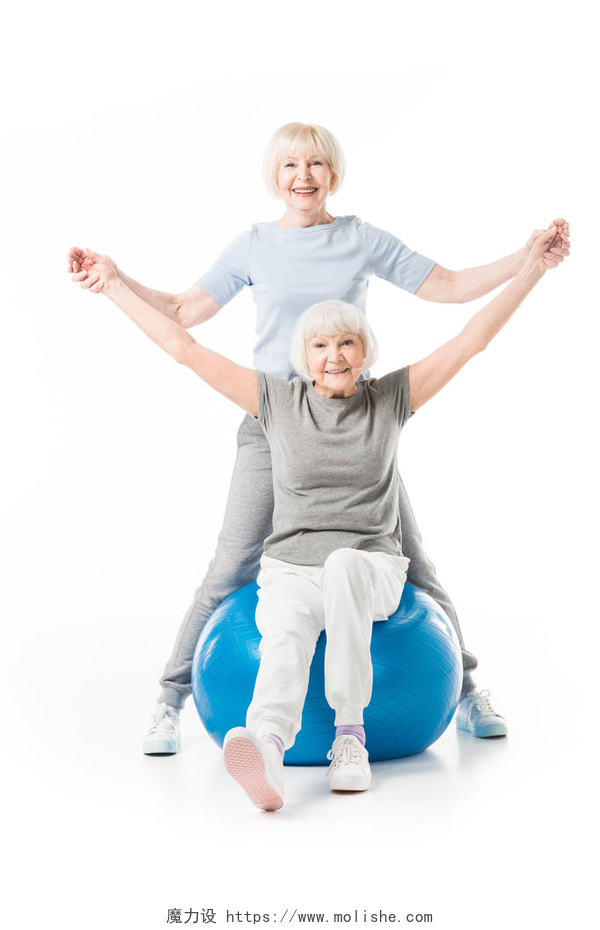 白色背景墙坐在瑜伽球的奶奶被另一个奶奶拉着手微笑高级运动员与健身球隔绝白色